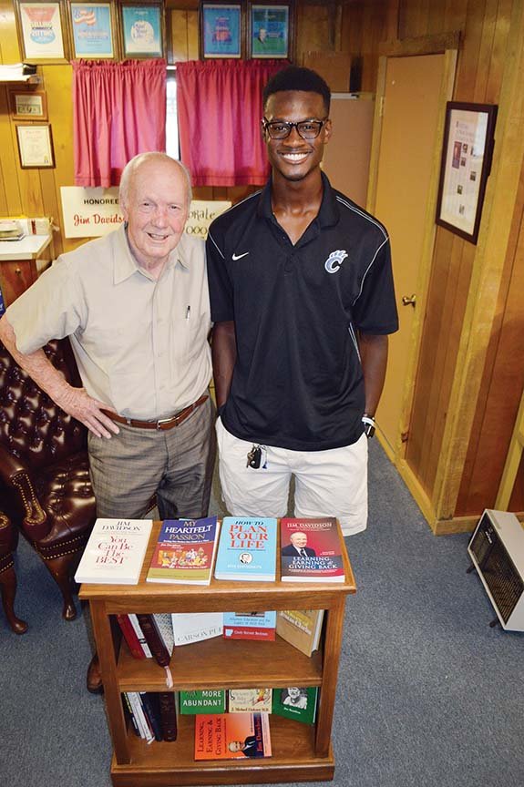 Jim Davidson, left, founder of the Conway Bookcase Project, stands in his home office with JoVoni Johnson, a senior at Conway High School and the recipient of a bookcase like the one shown. JoVoni, a National Merit Semifinalist and quarterback of the football team, said the personalized bookcase and starter set of books he received in Head Start sparked his love of reading. The annual Bookcase for Literacy Banquet, a fundraising event, is scheduled for 6:30 p.m. Thursday in the Bob and Betty Courtway Middle School Cafeteria in Conway.