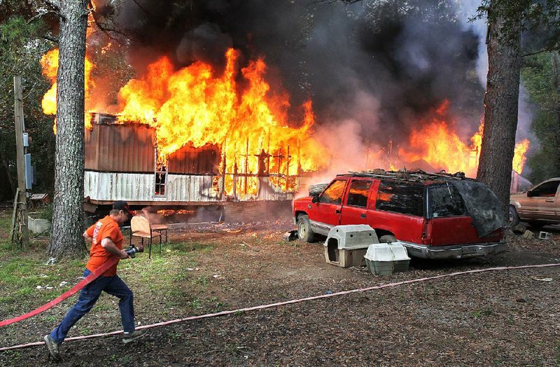 Piney Fire Department Chief Scott Miser pulls a hose into place near a mobile home in flames Tuesday near Royal. A 74-year-old man was found dead inside the destroyed structure. 