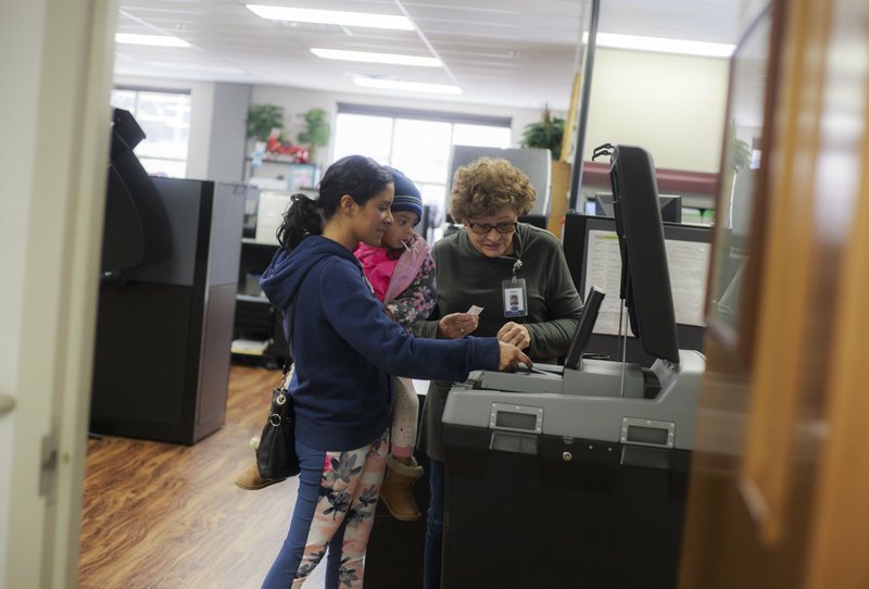 NWA Democrat-Gazette/CHARLIE KAIJO Deputy clerk Nancy McCloud (right) helps Regina Veliz of Bentonville with daughter Abby Veliz, 4, submit her voting sheet Friday at the Benton County Administration Office in Bentonville. Early voting in Benton and Washington counties hit record numbers.