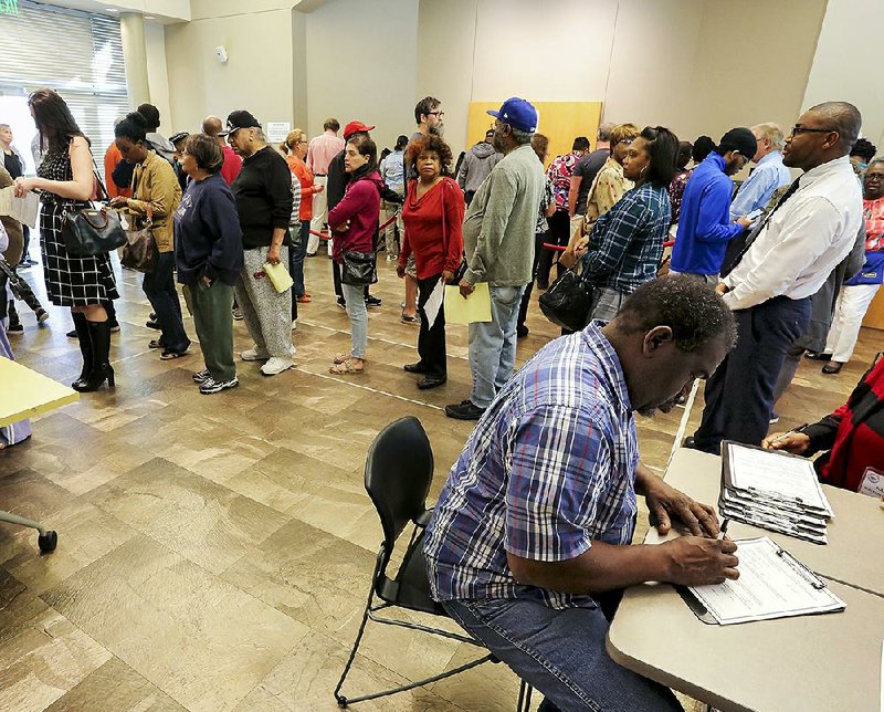 Jeffery Ridgle (bottom right) fills out paperwork Monday morning before getting in line for early voting at the Sidney S. McMath Library on John Barrow Road in Little Rock.