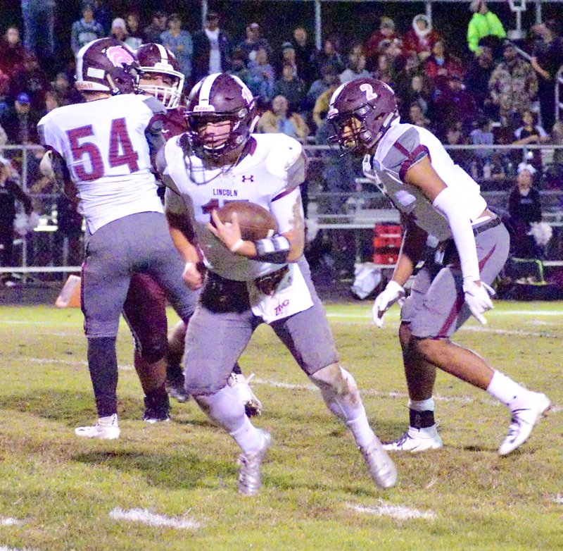 Westside Eagle Observer/RANDY MOLL With the blocking of Noah Moore (54) and Cam Brown (2), Lincoln quarterback Caleb Lloyd (15) looks to run through a hole in the Gentry line during play in Pioneer Stadium between Lincoln and Gentry on Friday, Oct. 26, 2018. Lloyd, a 4-year starter, is in his second year at quarterback.