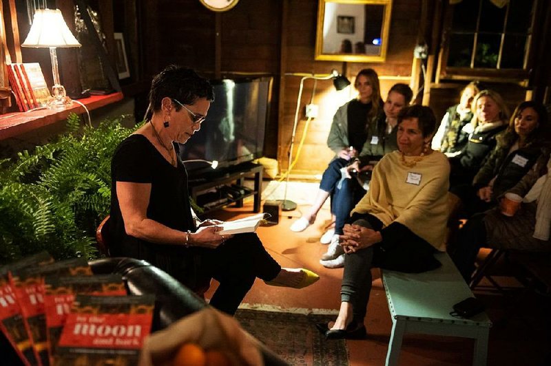 Lisa Kohn (left), a leadership consultant and coach from Wayne, Pa., reads an excerpt from her book, to the moon and back, at a gathering at home of neighbor Elaine Marnell (right).