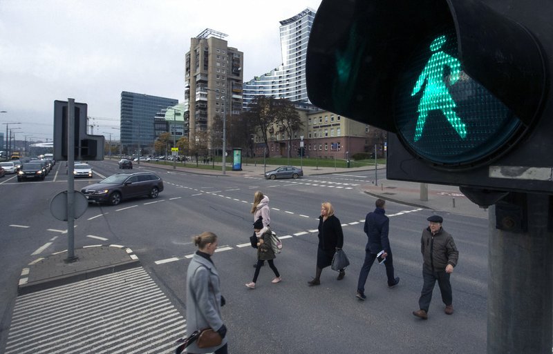 Pedestrians cross the street by traffic lights featuring a female figure on the green light, in Vilnius, Lithuania, Friday, Nov. 2, 2018. The Lithuanian capital has unveiled pedestrian crossing signals featuring women to mark the 100th anniversary of female suffrage. Vilnius mayor Remigjjus Simasius switched on the first 14 lights Friday - the centenary of the day when Lithuania’s Constitution was changed in 1918, allowing women the right to vote. (AP Photo/Mindaugas Kulbis)