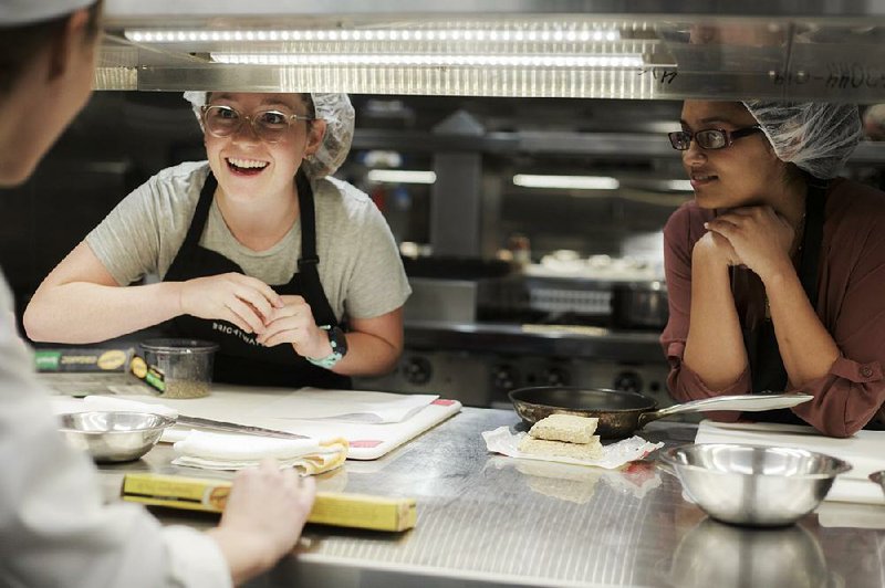 Medical student Emily Weldon (right) and pharmacy student Khusbu Bhikha take directions from chef instructor Erin Szopiak (left) during a cooking class Oct. 29 at Brightwater in Bentonville. 