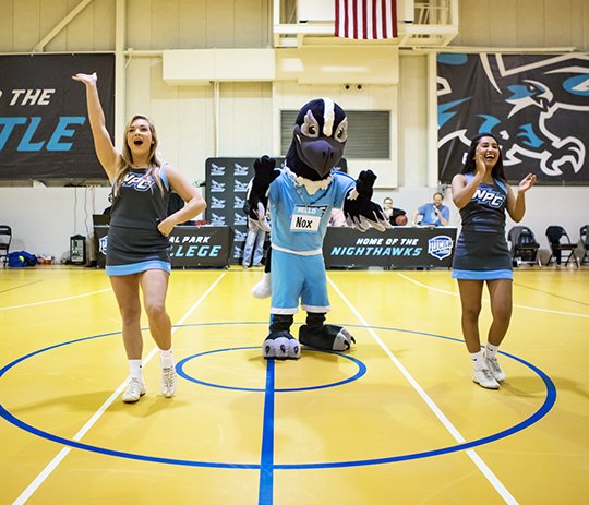 Submitted photo INTRODUCING NOX: During halftime of the men's basketball season opener Monday, National Park College officially named the beloved Nighthawk mascot, Nox, center, after the community submitted names and voted for their favorite. Cheer team members Brooke Neel, left, and CiCi Lopez helped Nox celebrate with the crowd during the halftime performance.