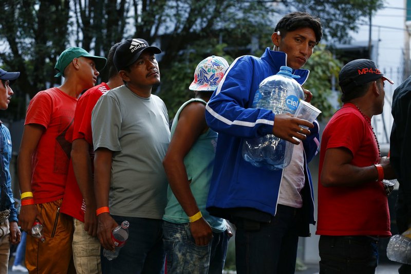 Men line up for donated drinking water, after scores of Central American migrants, representing the thousands participating in a caravan trying to reach the U.S. border, undertook an hours-long march to the office of the United Nations' humans rights body in Mexico City, Thursday, Nov. 8, 2018. Members of the caravan which has stopped in Mexico City demanded buses to take them to the U.S. border, saying it is too cold and dangerous to continue walking and hitchhiking.(AP Photo/Rebecca Blackwell)