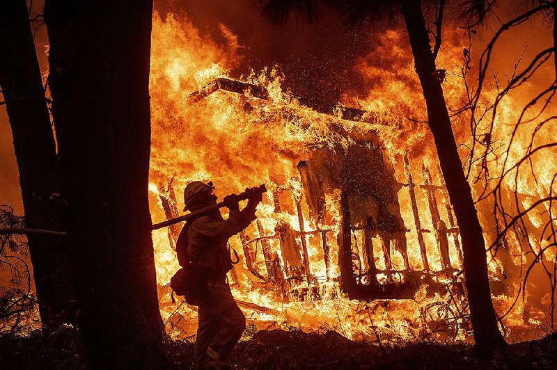 Firefighter Jose Corona watches a house go up in flames as he sprays water on it Friday in Magalia in Northern California. The town is north of Paradise and was threatened by the same wildfire. 