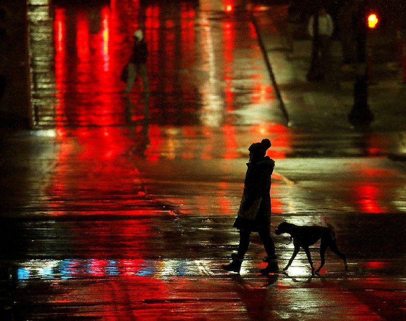 A woman and her dog cross a wet street as the first snow of the season in Missouri hits the pavement and melts in downtown Kansas City. 