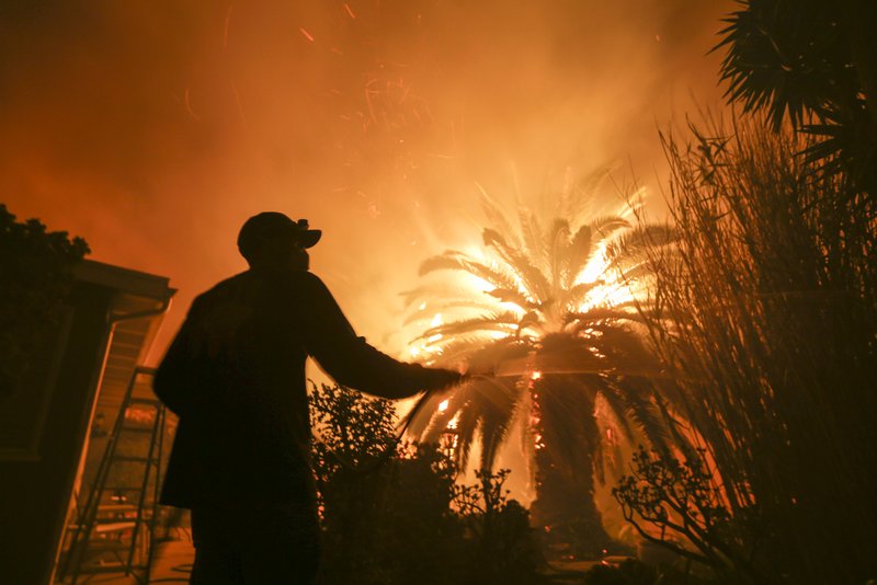Park Billow, 27, sprays water on the hot spots in his backyard Friday as the Woolsey Fire burns in Malibu, Calif. (AP Photo/Ringo H.W. Chiu)