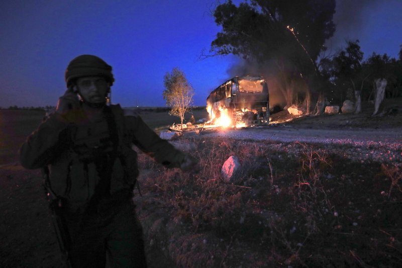 An Israeli soldier stands near a burning bus after it was hit by a mortar shell fired from Gaza near the Israel Gaza border, Monday, Nov. 12, 2018. Israeli media say six people were wounded by Palestinian fire, including a 19-year-old who was critically hurt when a mortar shell hit the bus. (AP&#xa0;Photo/Tsafrir Abayov)