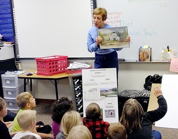 Lynn Atkins/Weekly Vista Xyta Lucas, president of the Bella Vista Historical Society, displays to a class of second graders at Cooper Elementary School a watercolor depicting the riding stable that was once on the land that later became the school.