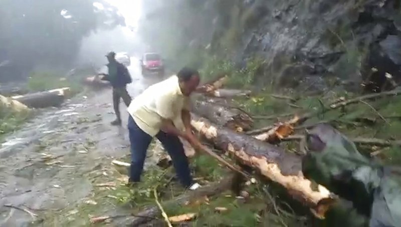 In this grab made from video provided by KK Productions, a man chops branches from a tree to clear a road after a cyclone struck Cuddalore, in the southern Indian state of Tamil Nadu, Friday, Nov. 16, 2018. A cyclone hit the coast of southern India on Friday, killing more than 10 people and damaging homes after more than 80,000 residents were evacuated. (KK Production via AP)