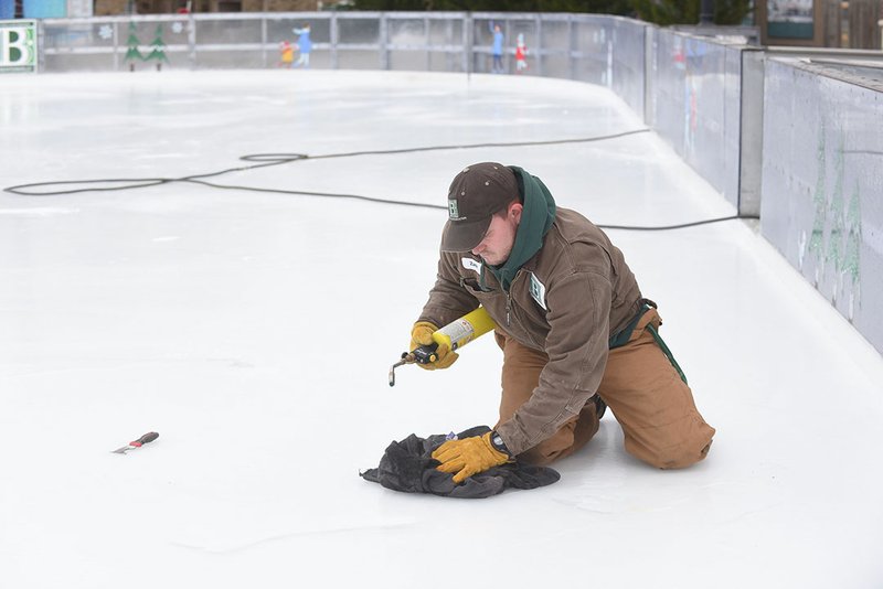 RINK READY NWA Democrat-Gazette/FLIP PUTTHOFF Zach Skinner with Bentonville Parks and Recreation smooths rough spots Wednesday at the Lawrence Plaza ice rink. The rink opens today. Skating is free from noon to 5 p.m. today, then the regular admission fees apply after 5 p.m.