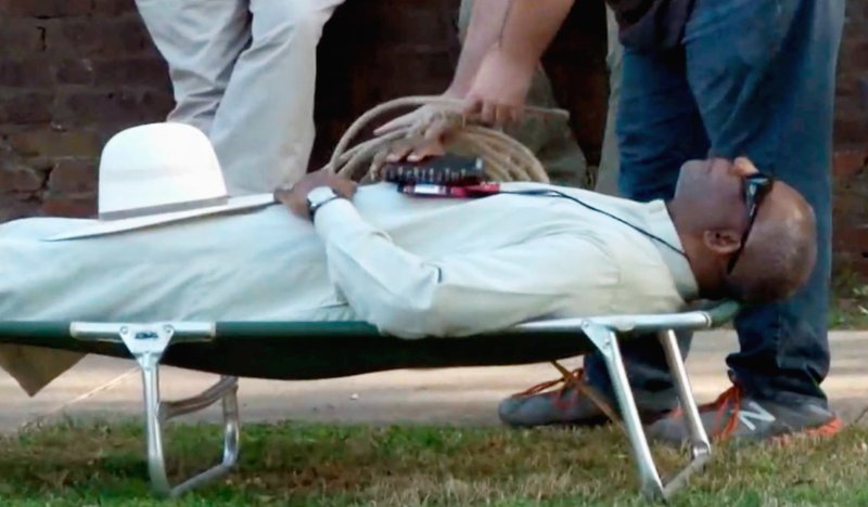FILE - In this April 17, 2018 file image from video provided by KTHV-TV, a death penalty protester outside the Arkansas governor's mansion in Little Rock prepares to tie rope around Pulaski County Circuit Judge Wendell Griffen who is laying on a cot in protest of executions. A disciplinary panel dismissed ethics charges Friday, Nov. 16, 2018, against the Arkansas Supreme Court's justices over their decision to prohibit Griffen from hearing any execution-related cases. The Arkansas Judicial Discipline and Disability Commission voted unanimously to dismiss the charges. (KTHV/TEGNA Inc. via AP, File)