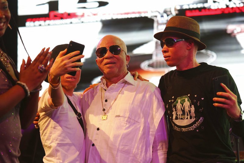 Salif Keita, center, takes a photo during a concert in Bamako, Mali, early Sunday, Nov. 18, 2018. Mali Singer and albino activist Salif Keita has dedicated a benefit concert to a 5-year-old albino girl who was kidnapped, tortured and killed in Mali in May. The concert on Saturday night Nov. 17, 2018, followed a forum on protecting albino people in Africa that Keita assembled. (AP Photo/Mohamed Kodio)