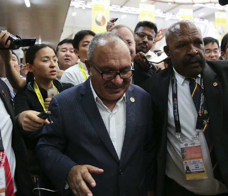 Papua New Guinea Prime Minister Peter O’Neill is escorted by se- curity Sunday as he is chased by reporters after reading a state- ment at the end of the APEC 2018 summit at Port Moresby, Papua New Guinea.