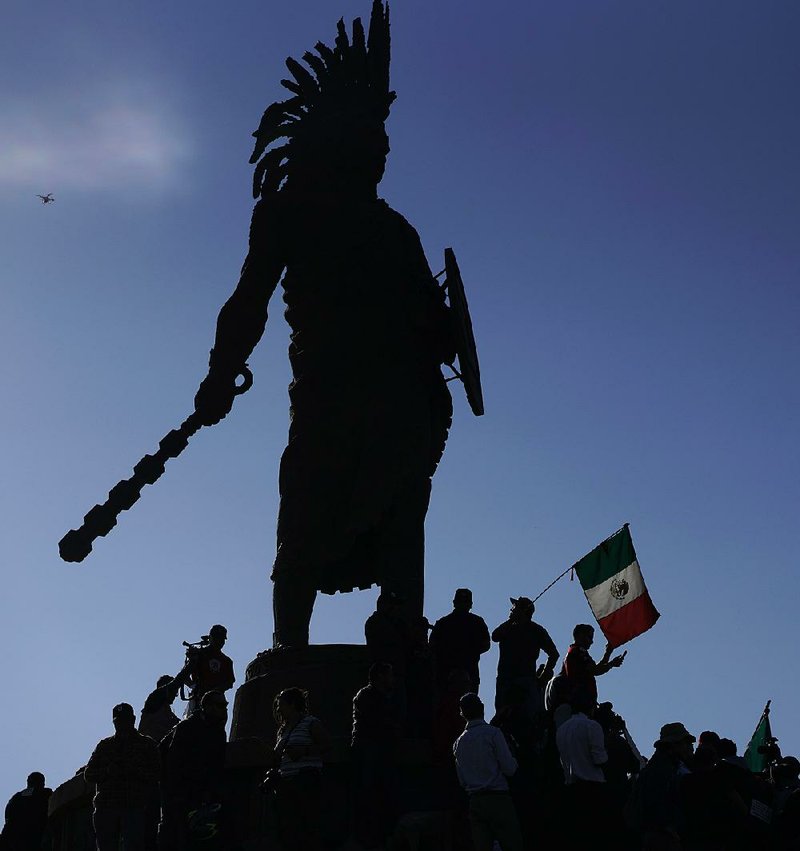 Demonstrators in Tijuana, Mexico, stand Sunday under a statue of Aztec ruler Cuauhtemoc as they protest the presence of Central American migrants. While the migrant caravan has received assistance from Mexicans for the past month, the mayor of Tijuana and some of its residents say the migrants are a problem for the city.