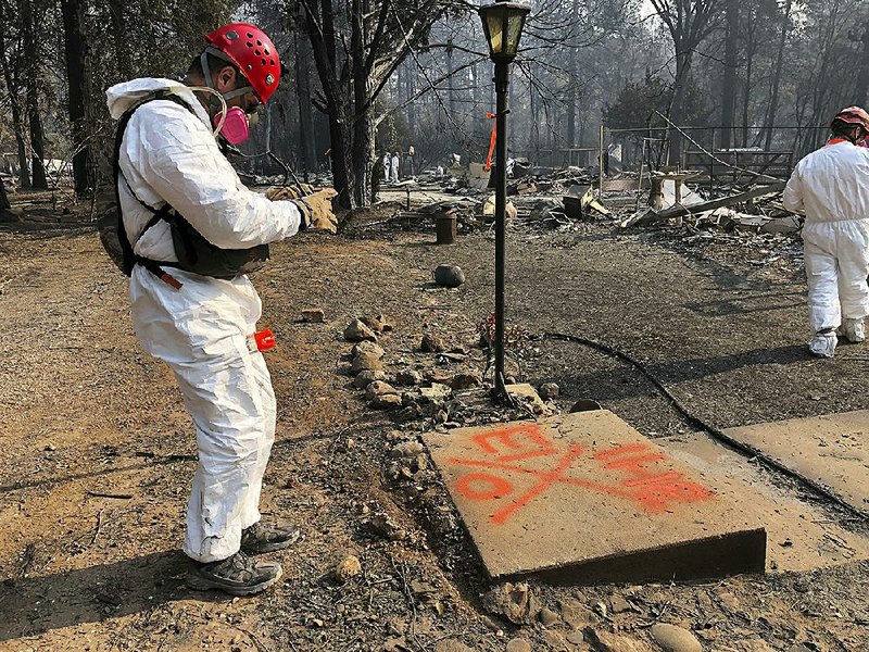 A volunteer member of an El Dorado County, Calif., search and rescue team takes a photo Sunday of the spray-painted symbols that show no human remains were found in the ruins of a home at that location in Paradise, Calif., destroyed by a wildfire.