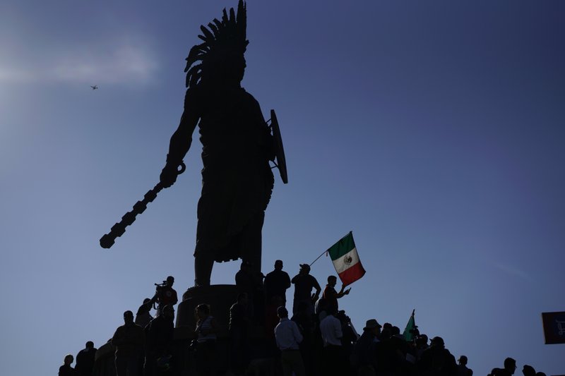 Demonstrators stand under an indigenous statue of Aztec ruler Cuauhtemoc as they protest the presence of thousands of Central American migrants in Tijuana, Mexico, Sunday, Nov. 18, 2018. Protesters accused the migrants of being messy, ungrateful and a danger to Tijuana; complained about how the caravan forced its way into Mexico, calling it an &quot;invasion,&quot; and voiced worries that their taxes might be spent to care for the group as they wait possibly months to apply for U.S. asylum. (AP Photo/Ramon Espinosa)