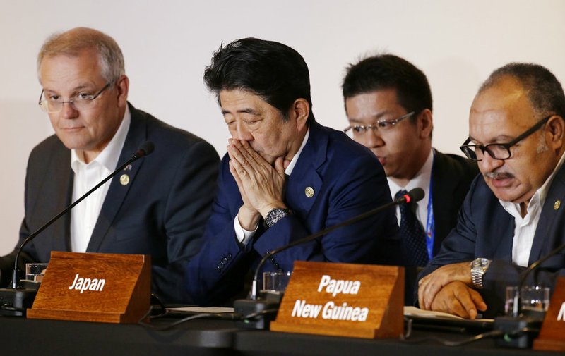 Japanese Prime Minister Shinzo Abe, center, gestures beside Australian Prime Minister Scott Morrison, left, and Papua New Guinea Prime Minister Peter O'Neill during the Leaders Electrification Project meeting as part of the APEC 2018 at Port Moresby, Papua New Guinea on Sunday, Nov. 18, 2018. In a statement issued to media, Papua New Guinea has invited Australia, Japan, New Zealand and the United States to work together to support its enhanced connectivity and the goal of connecting 70% of its population to electricity by 2030. Currently only about 13% of Papua New Guinea's population have reliable access to electricity. (AP Photo/Aaron Favila)