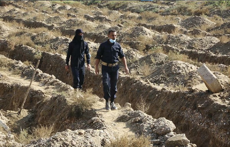 Syrian workers for a human-rights group walk through the site believed to be a mass grave containing the bodies of hundreds of people near Raqqa in northern Syria.