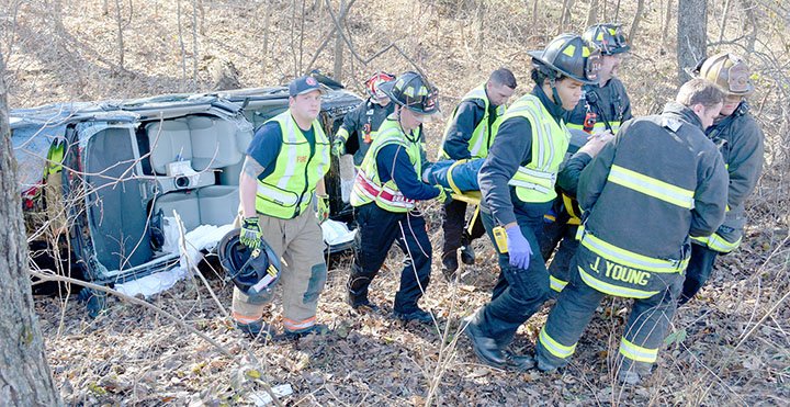 Keith Bryant/The Weekly Vista After extracting the patient at an accident site on Highlands Blvd., a group of firefighters carry him back up the ravine to a stretcher before loading him into the ambulance.