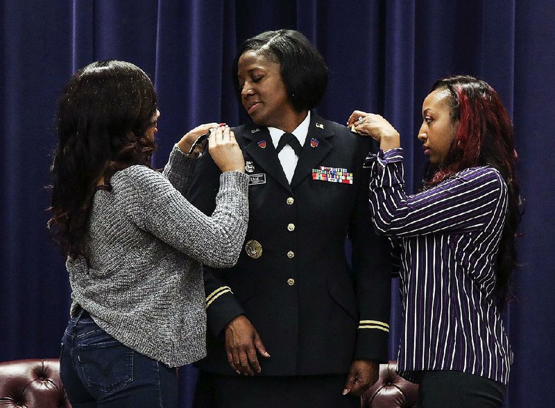 Col. Erica Ingram’s daughters Desarie Ingram (left) and DeeDee Shantelle pin insignias on Ingram’s uniform during a ceremony Thursday at Camp Robinson in North Little Rock.