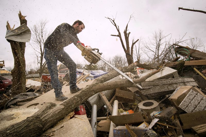 Steven Tirpak uses a chainsaw Sunday, Dec. 2, 2018, to remove tree branches that fell onto his two-story home in Taylorville, Ill. The National Weather Service says multiple tornadoes touched down in central Illinois, damaging dozens of structures and injuring multiple people. (Ted Schurter/The State Journal-Register via AP)