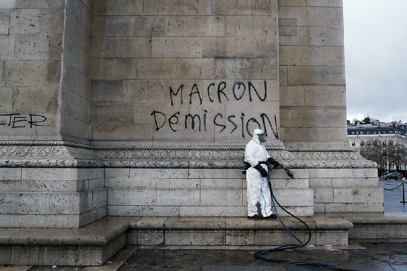 A worker prepares to clean graffiti from the Arc de Triomphe in Paris reading “Macron resignation” Sunday, the day after a riot over rising taxes and the high cost of living. 