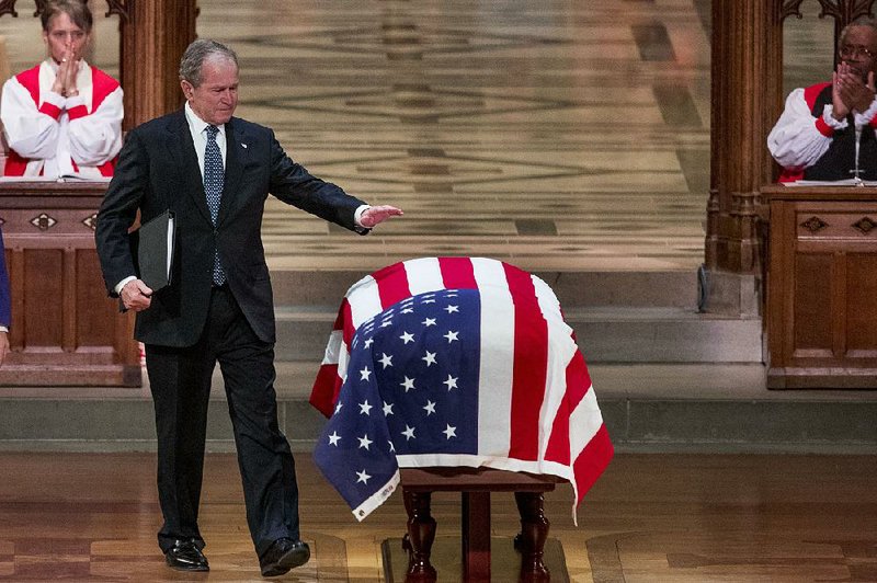 Former President George W. Bush touches his father’s flag-draped coffin Wednesday after sharing memories and stories about the elder Bush during a state funeral at Washington National Cathedral.