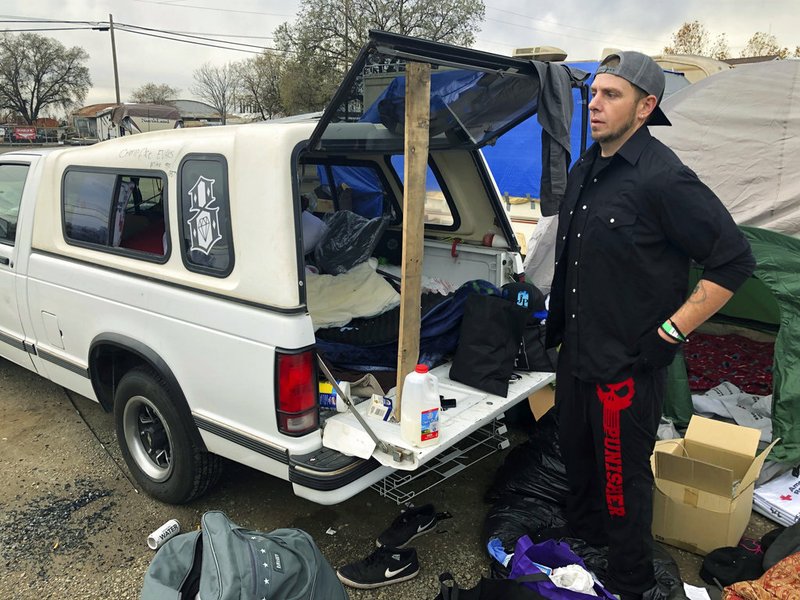In this Tuesday, Dec. 4, 2018 photo Michael Jones organizes a pile of donated blankets, sleeping bags and clothes in a fairgrounds parking lot that's become home to some of the people displaced by California's deadliest wildfire in Chico, Calif. Jones lost nearly everything he owns when the fire destroyed his trailer and his mom's home in Paradise last month, but he's determined to stay put because he doesn't want to be a burden on his friends and relatives. (AP Photo/Jonathan J. Cooper)