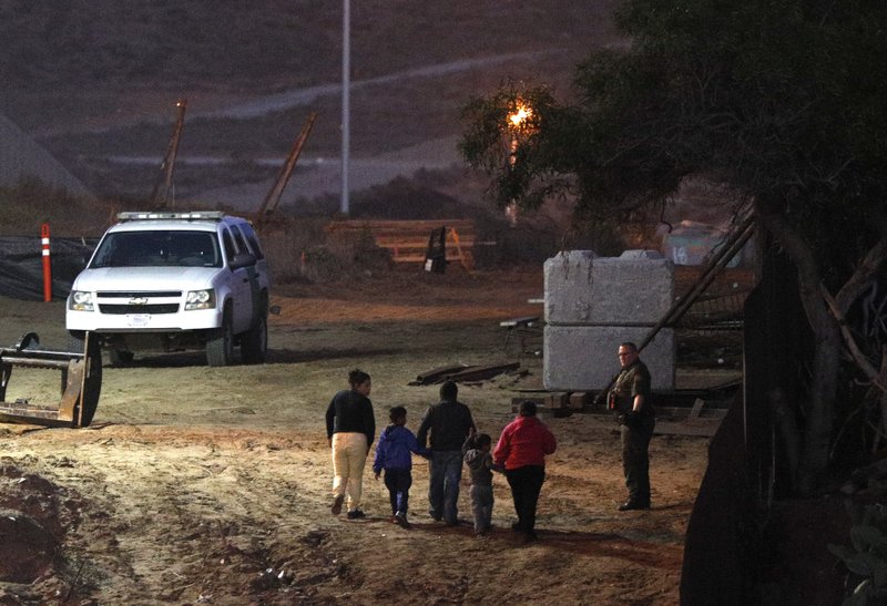 Migrants traveling with children walk up a hill to a waiting U.S. Border Patrol agent just inside San Ysidro, Calif., after climbing over the border wall from Playas de Tijuana, Mexico, on Dec. 3. Thousands of Central American migrants who traveled with recent caravans want to seek asylum in the United States but face a decision between crossing illegally or waiting months, because the U.S. government only processes a limited number of those cases a day at the San Ysidro border crossing. (AP Photo/Rebecca Blackwell)

