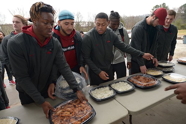 Mike Woods (from left), Isaiah Nichols and Devwah Whaley join other members of the University of Arkansas football team Thursday, Dec. 6, 2018, in serving a meal at the 7Hills Homeless Center's day center in Fayetteville. Members of the team served food at several locations around Northwest Arkansas including Arkansas Children's Hospital Northwest, Mercy medical center in Rogers and the Boys and Girls Club of Fayetteville.