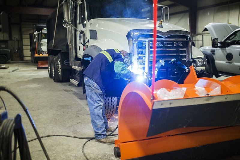 At the Benton County Road Department  in Bentonville, welder mechanic Derek Henson installs light bars Thursday above the  snowplow of a dump truck that will be used to plow the roads if  the forecast of snow proves correct. 