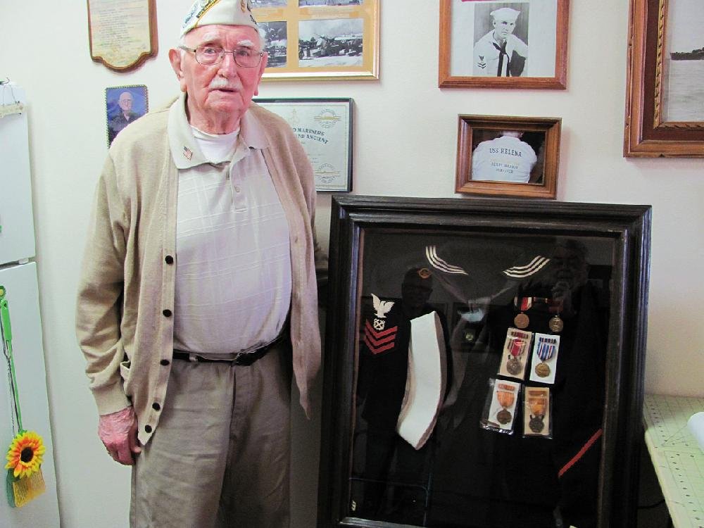 Harold Mainer of Fort Smith, who was at Pearl Harbor when the Japanese attacked on Dec. 7, 1941, shows the uniform he wore and the medals he was awarded for service aboard the USS Helena during the war. A photo of a young Mainer on the wall above the display was taken after the light cruiser Helena was sunk in battle in July 1943. 