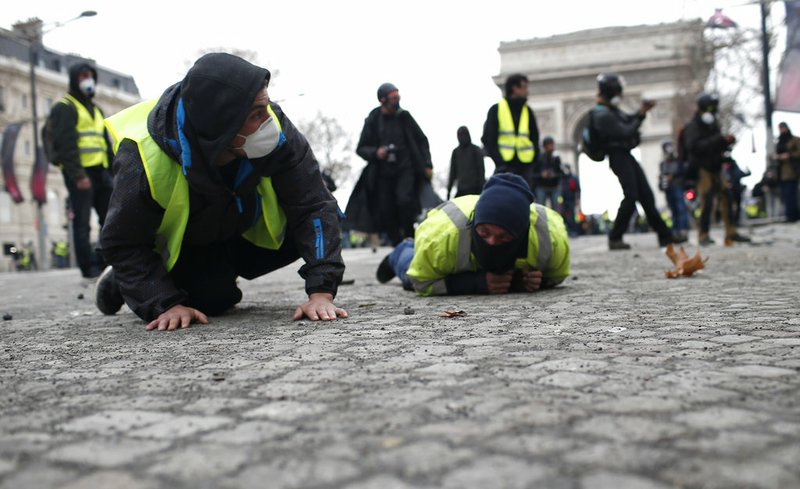 Demonstrators drop flat to the ground on the Champs-Elysees avenue during a protest Saturday, Dec. 8, 2018 in Paris. Crowds of yellow-vested protesters angry at President Emmanuel Macron and France's high taxes tried to converge on the presidential palace Saturday, some scuffling with police firing tear gas, amid exceptional security measures aimed at preventing a repeat of last week's rioting. (AP Photo/Rafael Yaghobzadeh)