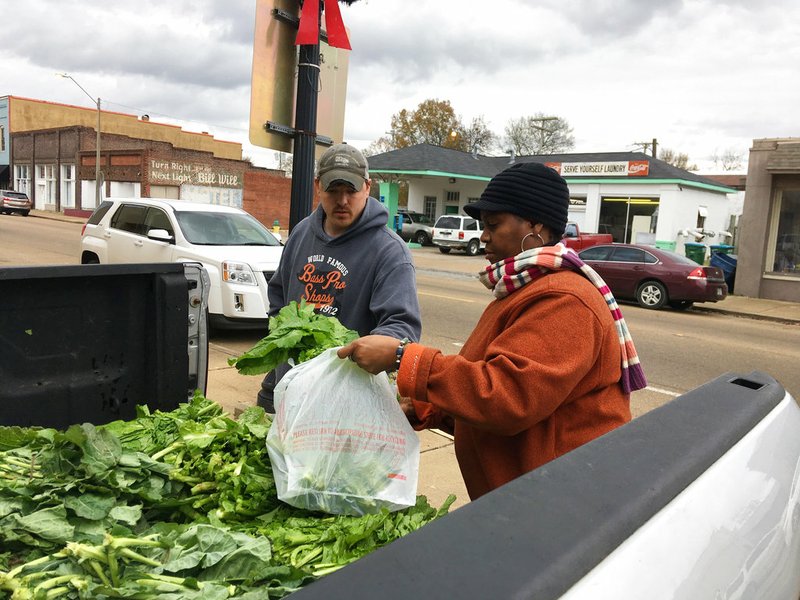 Zachary Osborne, left, buys mustard greens from Elaine Blair in Canton, Miss., on Friday, Dec. 7, 2018. Osborne and Blair each said people in Canton have been talking about voter fraud charges brought against seven people in connection to the 2017 Canton city elections. Six people were arrested Thursday, Dec. 6, 2018, and one Friday, Dec. 7. (AP Photo/Emily Wagster Pettus)