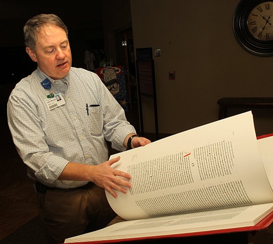 Father Michael Millard looks shows The Sentinel-Record the copy of the St. John's Iluminated Bible that is on display in the lobby of CHI St. Vincent Hot Springs Friday, December 7, 2018. (The Sentinel-Record/ichard Rasmussen)