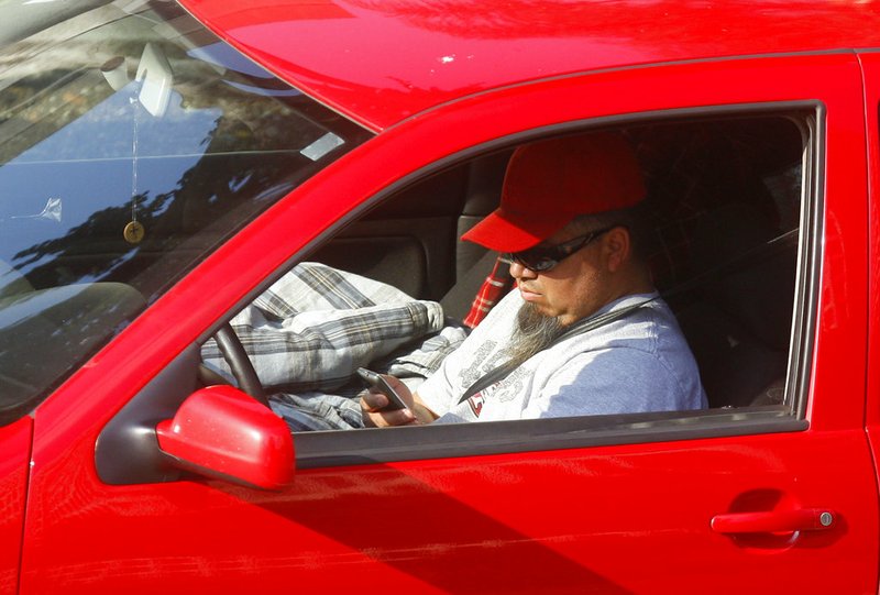 In this Dec. 14, 2011 file photo, a driver uses a cellphone while driving in Los Angeles. California regulators are considering a plan to charge a fee for text messaging on mobile phones to help support programs that make phone service accessible to the poor. The Mercury News said Wednesday, Dec. 12, 2018, the proposal is scheduled for a vote next month. (AP Photo/Damian Dovarganes, File)