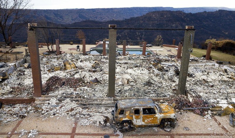 In this Dec. 3, 2018 file photo, a vehicle rests in front of a home leveled by the Camp Fire in Paradise, Calif. Authorities estimate it will cost at least $3 billion to clear debris of 19,000 homes destroyed by California wildfires last month. State and federal disaster relief officials said Tuesday, Dec. 11, 2018, that private contractors will most likely begin removing debris in January from Butte, Ventura and Los Angeles counties and costs are likely to surpass initial estimates. (AP Photo/Noah Berger, File)