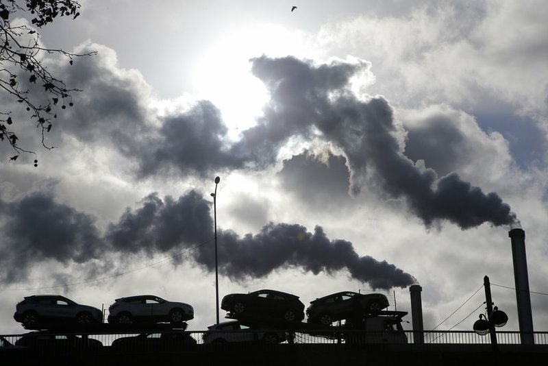 In this Friday, Nov. 30, 2018 file photo smoke rises from a factory as a truck loaded with cars crosses a bridge in Paris, France. (AP Photo/Michel Euler, File)