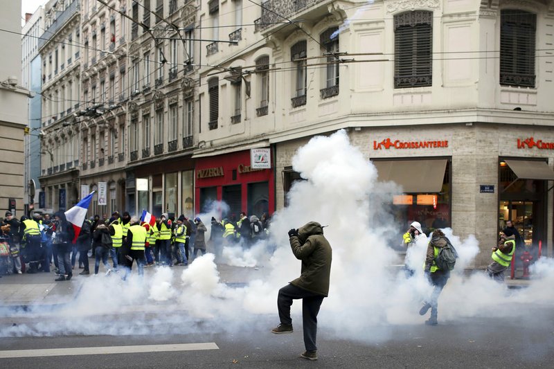 Demonstrators run away through tear gas in Lyon, central France, Saturday, Dec. 15, 2018. The demonstrations against France's high cost of living, sapped by cold weather, rain and recent concessions by French President Emmanuel Macron, were significantly smaller Saturday than at previous rallies. (AP Photo/Laurent Cipriani)