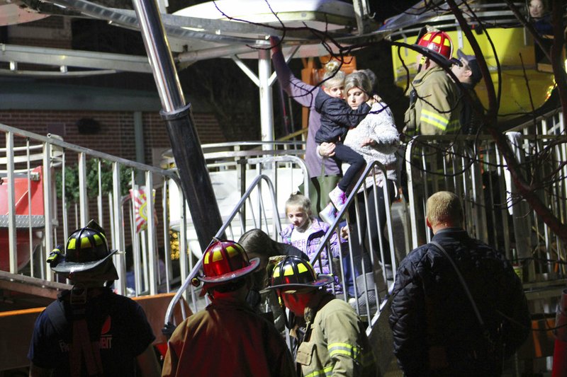 In this Saturday, Dec. 15, 2018, photo, firefighters help passengers off of a Ferris wheel that malfunctioned in downtown Conway, Ark. A pivot pin holding one of the Ferris wheel's cylinders in place broke. All passengers were safely rescued. (Jeanette Anderton/Log Cabin Democrat via AP)