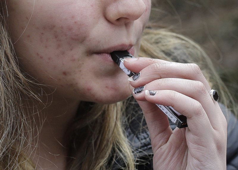 FILE - In this April 11, 2018 file photo, a high school student uses a vaping device near a school campus in Cambridge, Mass. Twice as many high school students used nicotine-tinged electronic cigarettes in 2018 compared with the previous year, an unprecedented jump in a large annual survey of teen smoking, drinking and drug use. Findings were released on Monday, Dec. 17, 2018. (AP Photo/Steven Senne, File)