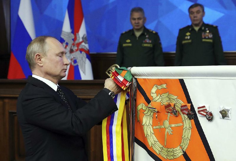Russian President Vladimir Putin pins a medal on a military banner during a Tuesday meeting with top military staff members in the Russian Defense Ministry’s headquarters in Moscow. 