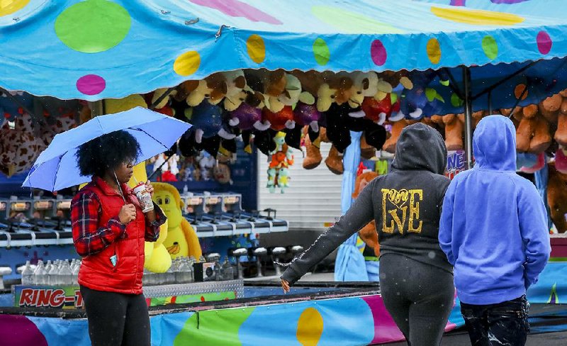 Jasmine Jones (left) of Little Rock waits in the rain for her daughter to finish a ride at the Arkansas State Fair on Oct. 15. Fair officials said persistent rain caused an operating shortfall at this year’s event, and lawmakers endorsed a plan Wednesday to allocate up to $911,050 in rainy-day funds to cover the losses. 