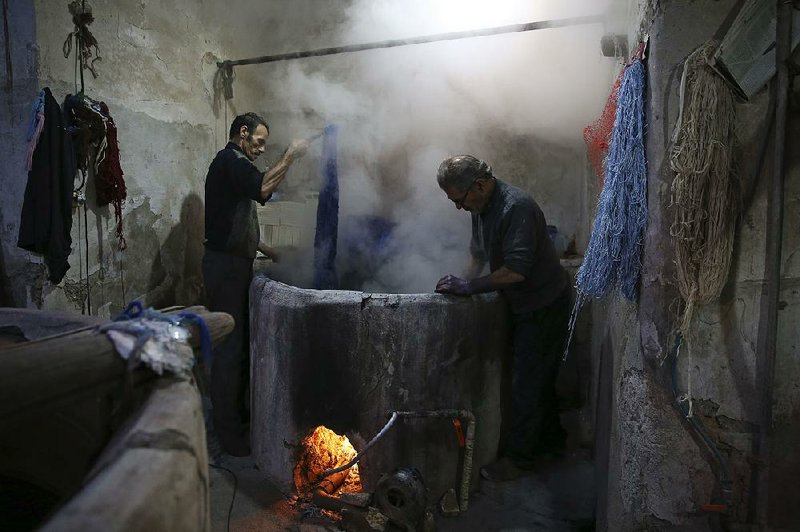 Steam rises from a vat of dye as a batch of thread is prepared in a carpet workshop at the Kashan bazaar. 