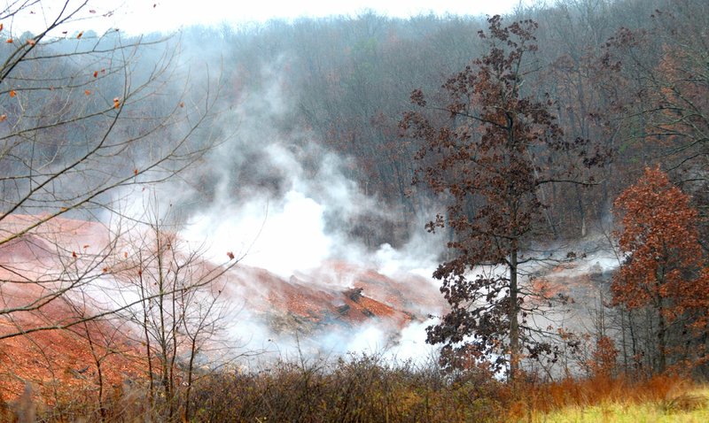 NWA Democrat-Gazette/DAVID GOTTSCHALK Smoke rises Friday, Dec. 14, from an underground fire at the former "stump dump" site on Trafalgar Road in Bella Vista. The site was once a Bella Vista Property Owners Association "stump dump" at which residents of the city could dump yard waste.