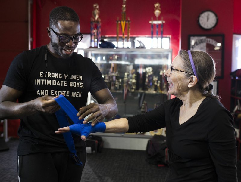 NWA Democrat-Gazette/CHARLIE KAIJO Strightright boxing coach Bernard Oliver puts hand wraps on the hands of Jonelle Lipscomb (from left) during a boxing class geared towards people with Parkinson's disease, Monday, December 10, 2018 at Straightright Boxing and Fitness Springdale.