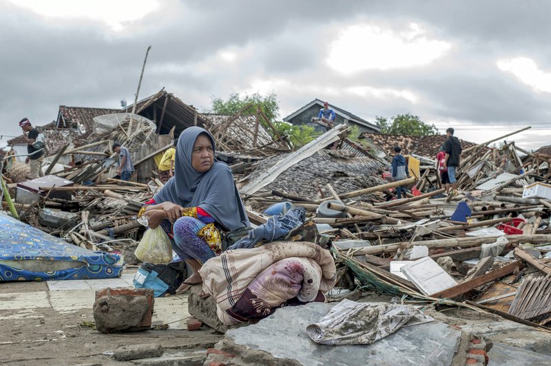 A tsunami survivor sits on a pice of debris as she salvages items from the location of her house in Sumur, Indonesia, Monday, Dec. 24, 2018. Doctors worked to save injured victims while hundreds of military and volunteers scoured debris-strewn beaches in search of survivors Monday after a deadly tsunami gushed ashore without warning on Indonesian islands on a busy holiday weekend. (AP Photo/Fauzy Chaniago)